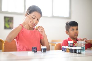 Une fille et un garçon peignant des fibules, des bijoux qu'ils ont créer.